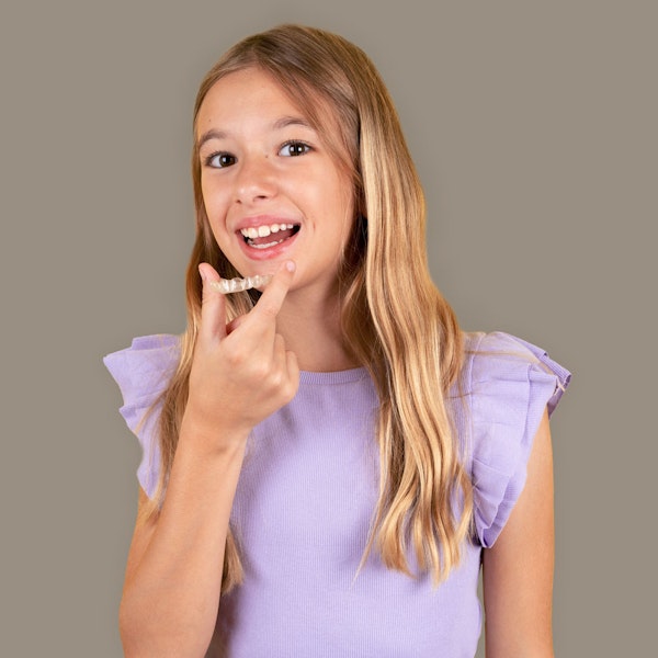 Smiling young girl holding an Invisalign aligner